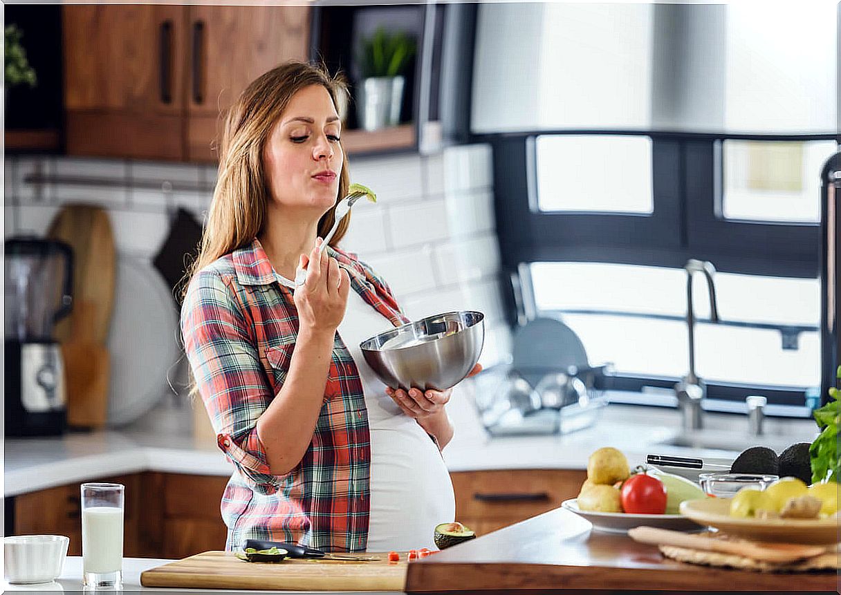 A pregnant woman eating in her kitchen. 