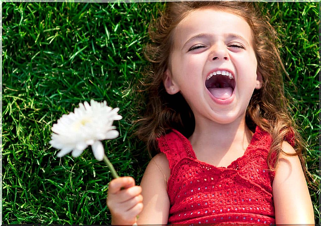 A young girl lying in the grass with a flower in her hand. 