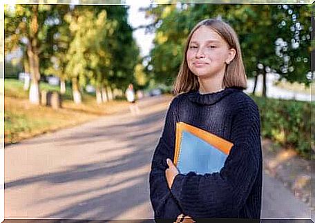 A smiling teenage girl with books in her arms. 