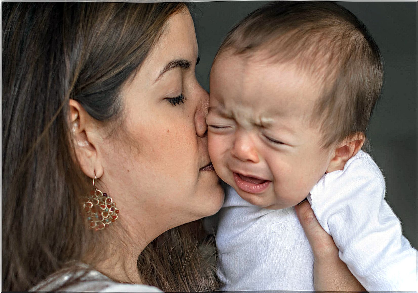 A crying baby kissed by his mom