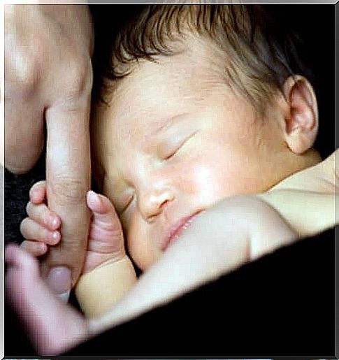 A newborn baby gripping an adult's finger. 